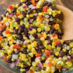Corn and Black Bean Salad with Mexican Vinaigrette in a glass bowl with bell peppers, red onion, and cilantro, ready to serve.