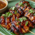 Filipino Chicken Barbecue skewers coated in a sticky sweet and savory glaze, grilled with smoky char marks and garnished with green onions and cilantro.