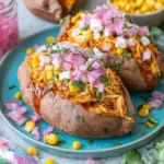 BBQ Chicken Stuffed Sweet Potatoes topped with shredded BBQ chicken, pickled red onions, sweet corn, and fresh cilantro on a blue plate.