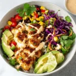 Baja Fish Taco Bowls topped with blackened cod, creamy sauce drizzle, purple cabbage slaw, corn, black beans, avocado, cilantro, and lime.
