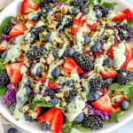 Berry Salad with Creamy Lemon Herb Dressing in a white bowl with mixed greens, strawberries, blueberries, blackberries, purple cabbage, crunchy seeds, and creamy herb drizzle.