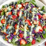 Berry Salad with Creamy Lemon Herb Dressing in a white bowl with mixed greens, strawberries, blueberries, blackberries, shredded purple cabbage, nuts, and creamy herb drizzle.