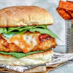 Buffalo Chicken Burgers topped with melted blue cheese, fresh spinach, and buffalo sauce on a toasted bun with crispy sweet potato fries.