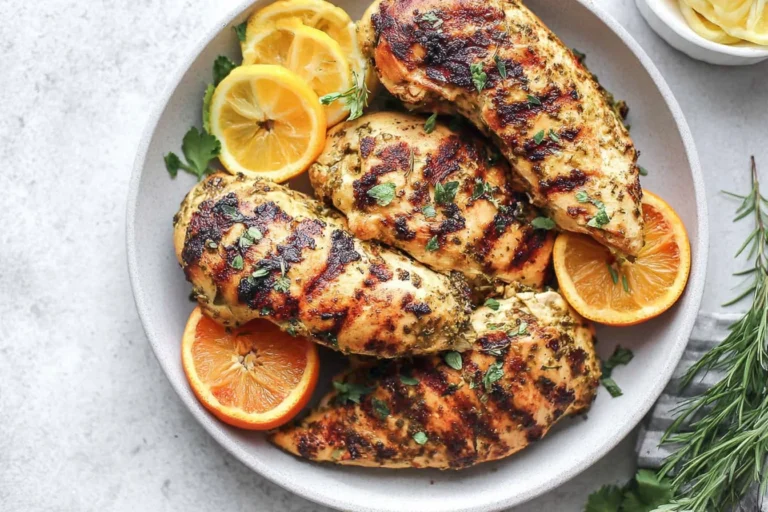 Citrus Dijon Grilled Chicken on a plate with orange and lemon slices, grilled char marks, and fresh herbs.