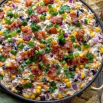 Creamy Cowboy Corn Dip topped with crispy bacon, black beans, sweet corn, green onions, and jalapeños, served with tortilla chips