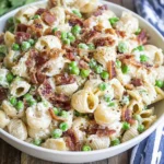 Creamy Pasta Salad with shell pasta, peas, crispy bacon, and parmesan in a creamy mayo dressing, served in a white bowl.