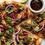 Close-up of Crispy Oven-Baked Birria Pizza with shredded beef birria, melted cheese, red onion, cilantro, and birria consommé for dipping