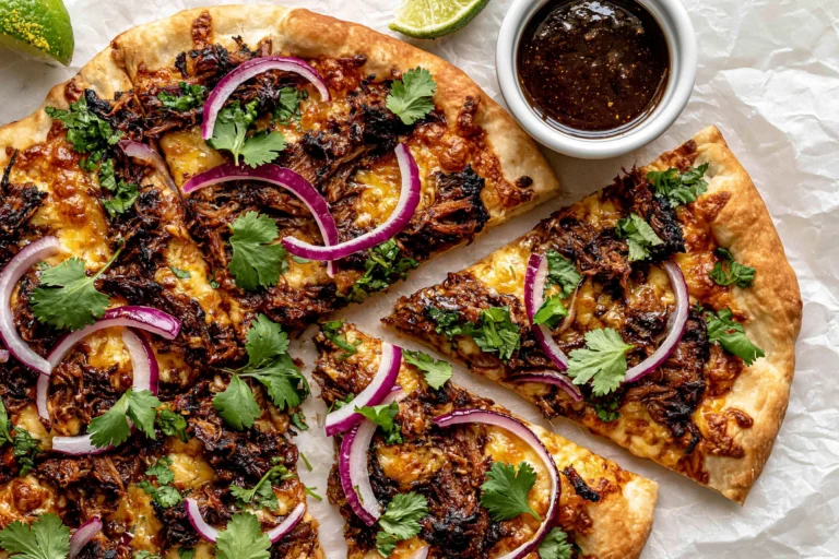 Close-up of Crispy Oven-Baked Birria Pizza with shredded beef birria, melted cheese, red onion, cilantro, and birria consommé for dipping