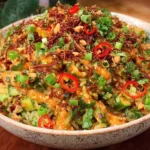Crispy Rice Salad with Peanut-Chili Dressing topped with herbs, peanuts, and sliced red chili in a bowl.