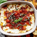 Baked Goat Cheese Bruschetta Dip baked until bubbly in a white casserole dish, topped with cherry tomatoes, basil ribbons, and balsamic drizzle with toasted crostini.