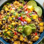 Fiesta Mango Quinoa Salad topped with cilantro, black beans, diced mango, jalapeño slices, and lime wedges in a blue bowl.