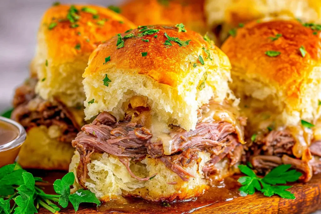Close-up of French Dip Sliders on buttery Hawaiian rolls with tender roast beef, melted provolone, herbs, and au jus for dipping.