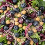 Chickpea Blueberry Salad with fresh blueberries, chickpeas, mixed greens, red onion, seeds, and creamy tahini dressing in a vibrant summer salad bowl