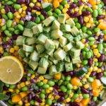 Edamame Mango Salad with avocado, black beans, corn, cucumber, and red onion in a colorful bowl with fresh lemon slices.
