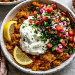 Golden Ground Turkey and Rice Skillet served in a bowl with seasoned golden rice, creamy garlic yogurt sauce, fresh cucumber tomato salad, red onion, parsley, and lemon wedges.