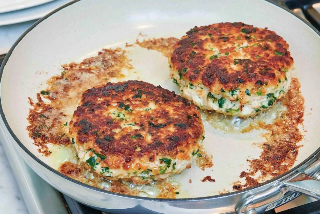 Greek Feta Turkey Burgers cooking in a skillet, featuring juicy turkey patties mixed with feta cheese, herbs, garlic, and fresh Mediterranean seasonings.