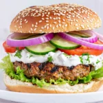 Greek Feta Turkey Burgers topped with creamy tzatziki, cucumber slices, tomatoes, red onion, and lettuce on a sesame seed bun.