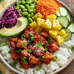 Hawaiian Chicken Poke Bowl with sticky glazed chicken, jasmine rice, pineapple, avocado, cucumber, edamame, carrots, and spicy mayo.