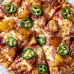 Hawaiian pizza with caramelized pineapple, smoky prosciutto, melted mozzarella, and fresh jalapeño slices on a crispy homemade pizza crust.