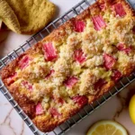 Lemon Rhubarb Bread with fresh rhubarb pieces and a golden, buttery crumb cooling on a wire rack with fresh lemons.