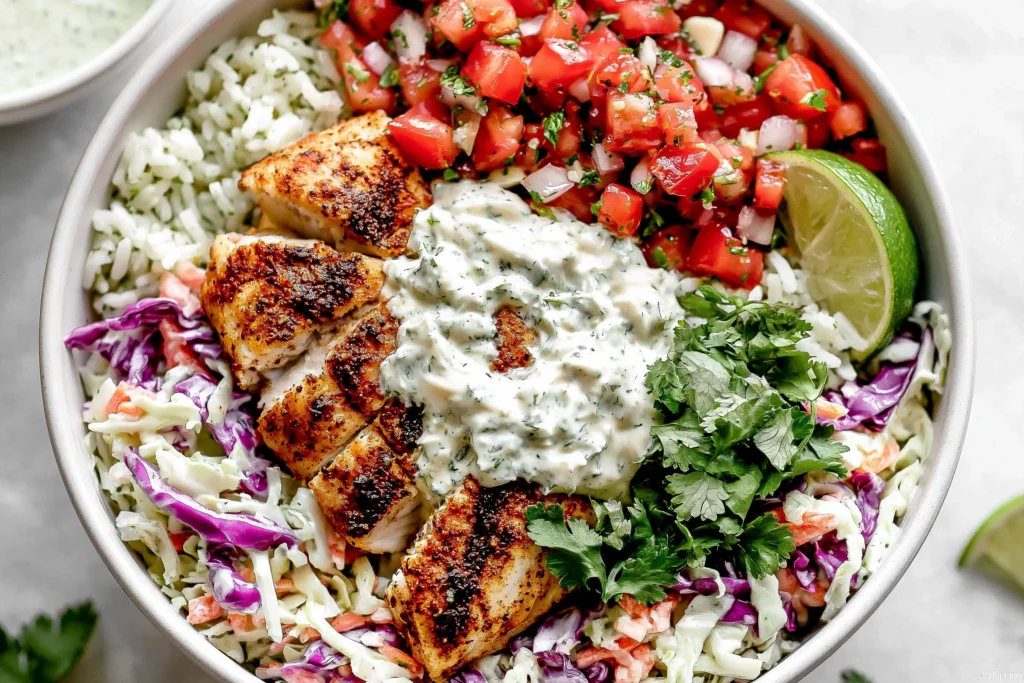 Mahi Mahi Taco Bowls topped with seasoned air-fried mahi mahi, cilantro lime crema, pico de gallo, cabbage slaw, cilantro lime rice, fresh cilantro, and lime wedges.