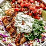 Mahi Mahi Taco Bowls topped with seasoned air-fried mahi mahi, cilantro lime crema, pico de gallo, cabbage slaw, cilantro lime rice, fresh cilantro, and lime wedges.