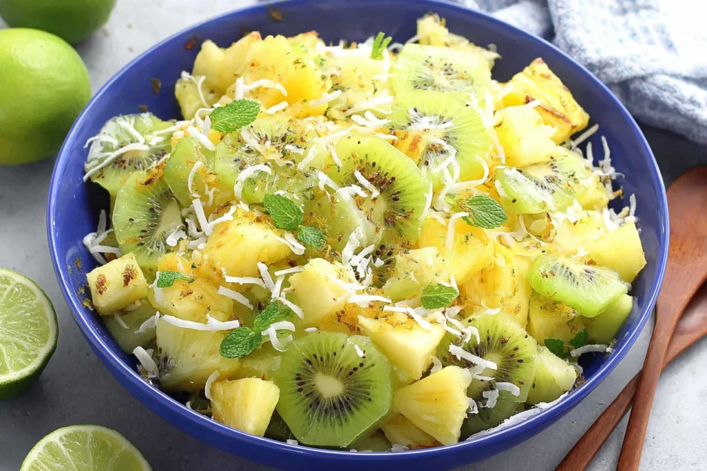 Pineapple Kiwi Salad in a blue bowl with honey-lime glaze, fresh mint, and toasted coconut.