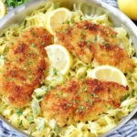 Crispy Romano Chicken with Lemon Garlic Pasta in a skillet with lemon wedges and parsley over buttery linguine.