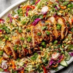 Sesame Chicken Cabbage Crunch Salad with sliced grilled sesame chicken, crunchy cabbage, carrots, peppers, herbs, and sesame ginger dressing on a platter.