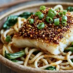 Sesame-Crusted Cod with Ginger Noodles served with crispy sesame-coated cod, tender ginger noodles, spinach, and fresh spring onions.