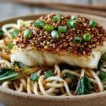 Sesame-Crusted Cod with Ginger Noodles featuring flaky sesame-crusted cod over savory ginger noodles with bok choy and fresh green onions.