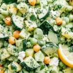 Sunshine Salad with chickpeas, cucumber, avocado, fresh herbs, and creamy citrus dressing, topped with feta cheese and served with lemon.