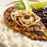 The Best Cuban Chicken served with white rice, black beans, caramelized onions, and fresh lime wedges for a classic Cuban-inspired meal.