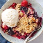 Mixed Berry Crisp in a bowl with vanilla ice cream, bubbly mixed berries, and golden oat streusel topping.