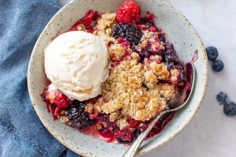 Mixed Berry Crisp in a bowl with vanilla ice cream, bubbly mixed berries, and golden oat streusel topping.