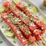Watermelon Tajin Skewers topped with lime, cotija cheese, mint, and flaky salt on a platter for a fresh, spicy-sweet summer snack.