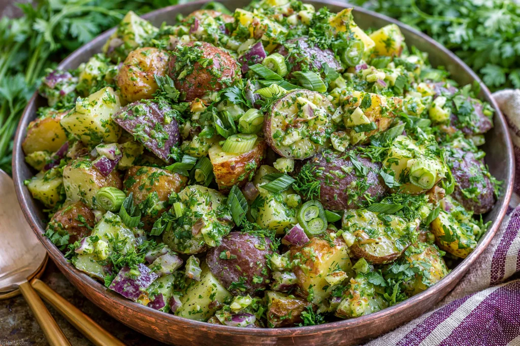 French Potato Salad with fresh herbs, Dijon mustard, green onions, and red potatoes in a tangy vinaigrette, served in a rustic bowl.