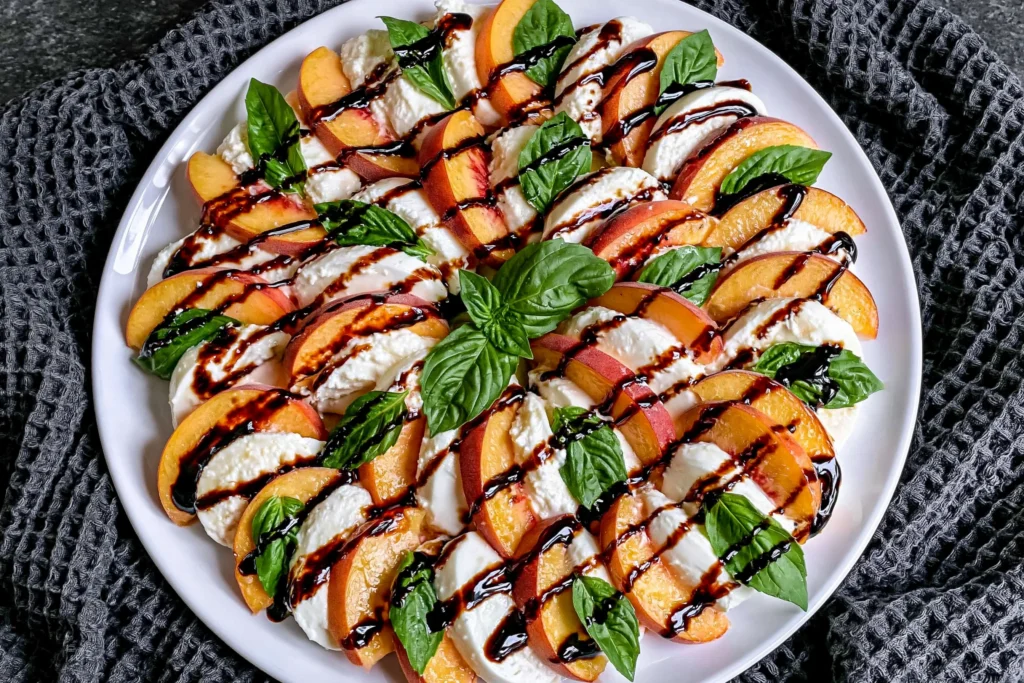 Peach Caprese Salad made with juicy fresh peaches, creamy mozzarella, basil leaves, and balsamic glaze on a serving platter.