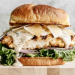 Grilled Chicken Caesar Burger on a toasted brioche bun with crisp lettuce, red onion, creamy Caesar dressing, shaved Parmesan, and juicy grilled chicken.