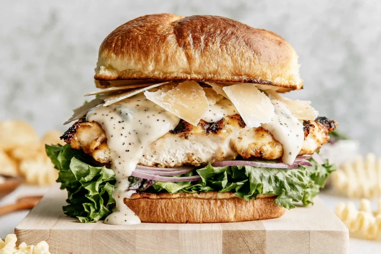 Grilled Chicken Caesar Burger on a toasted brioche bun with crisp lettuce, red onion, creamy Caesar dressing, shaved Parmesan, and juicy grilled chicken.