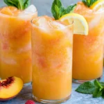 Peach Lemonade served over ice with fresh peach slices, lemon wedges, and mint leaves for a refreshing homemade summer drink.
