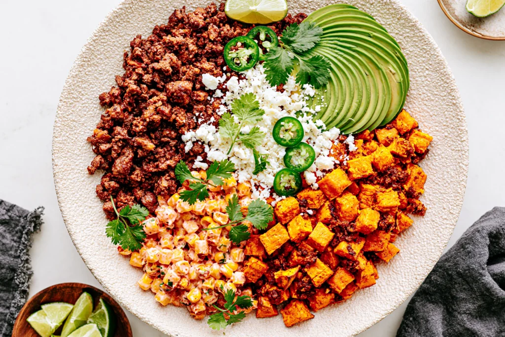 Street Corn Beef Bowl with seasoned ground beef, roasted sweet potatoes, creamy Mexican street corn, avocado, cotija cheese, jalapeños, and fresh cilantro.