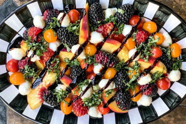 Summer Fruit Caprese Salad with peaches, heirloom tomatoes, fresh mozzarella, basil, blackberries, raspberries, and balsamic glaze on a serving platter.